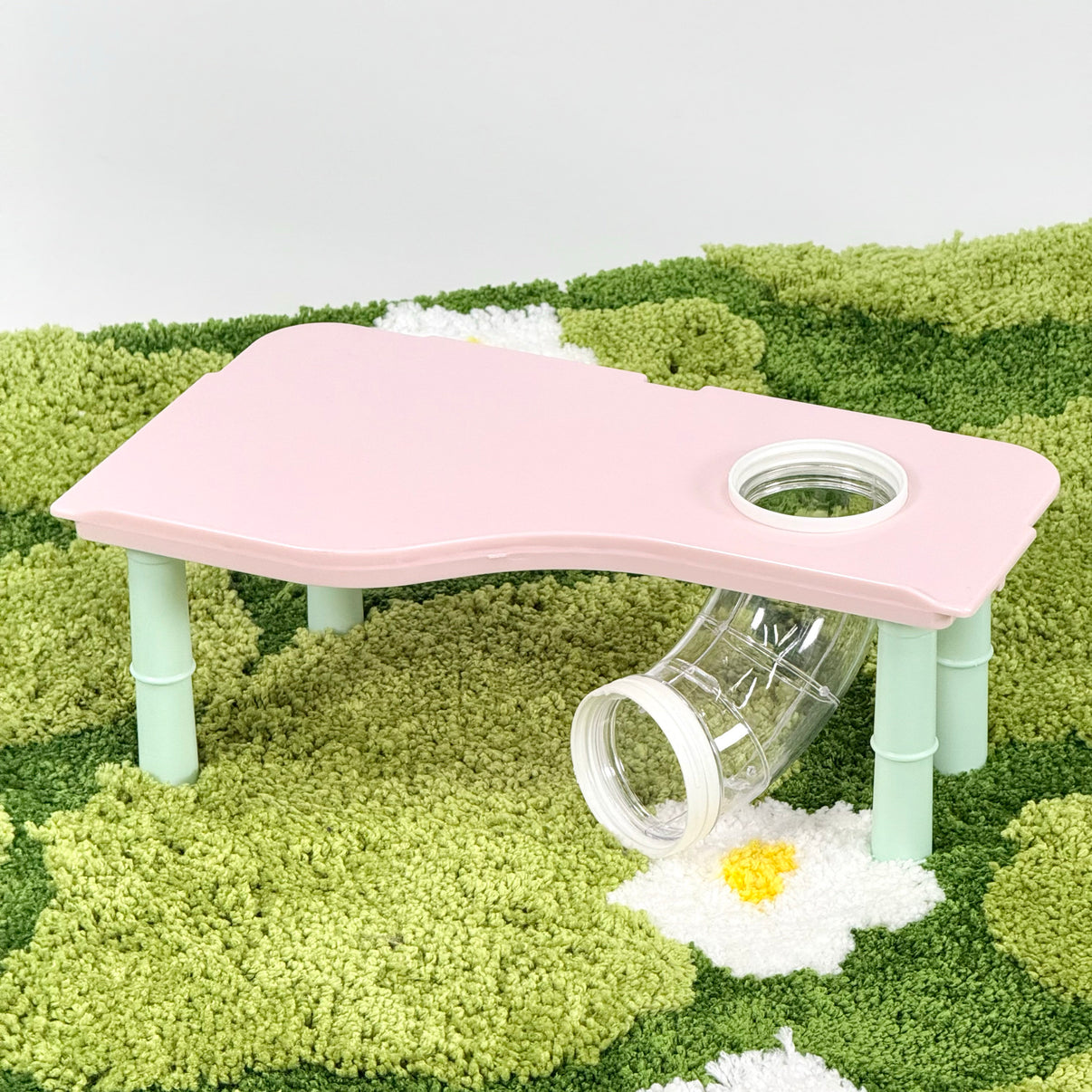 Pink plastic hamster hideout platform with tunnel on green textured mat